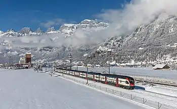 Train on tracks in valley between mountains with double-tracked railway line down the middle and snow on the ground