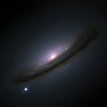 A dusty spiral galaxy seen close to edge-on against a black background, with a bright point of white at lower left