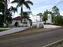 Small house surrounded by palm trees, with a Sabesp logo on its wall and a water tank and another building next to it