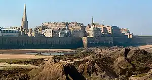 A view of a walled coastal city containing multi-level houses and apartments.