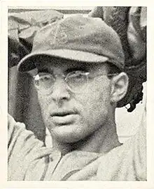 A man wearing glasses and a dark baseball cap with an overlapping "STL" on the front has his hands behind his head as if preparing–throw a ball.