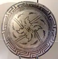 Samarra plate, with a design consists of a rim, a circle of eight fish, and four fish swimming towards the center being caught by four birds, at the center being a swastika symbol; circa 4000 BC; painted ceramic; diameter: 27.7 cm; Vorderasiatisches Museum (Berlin)