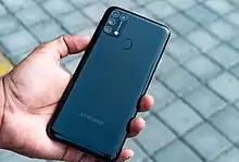 An oblong rectangular device, some 16 by 7.5 cm in size, resting easily in the palm of an adult hand. The rear of the phone is black and has four camera lenses in the upper left corner, with the name "SAMSUNG" in gray lettering centered near the bottom.