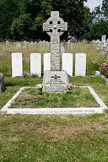 Photograph of a gravestone in front of a Celtic cross.