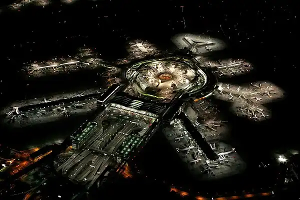 The building of an airport at night with a large central building with several lit spokes of the terminals.