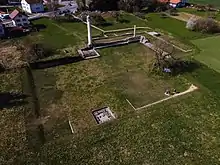 View from above a field with several ruined walls and two white columns.