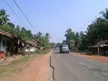 Dirt-shouldered road with buildings, two trucks and a motorbike