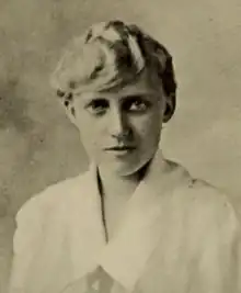 A young white woman with blond hair arranged across her forehead, wearing a white collared blouse