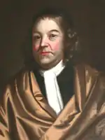 A head and shoulders portrait of Bradstreet, who wears a gold-peach robe over a black shirt and white cravat. His shoulder-length hair is topped with a small black cap.