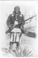 "Scene in Geronimo's camp...before surrender to General Crook, March 27, 1886: Geronimo, full-length portrait standing, facing left, rifle at port."