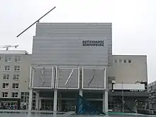 The outside of the theatre. A brutalist building with a sign saying "ROTTERDAMSE SCHOUWBERG".