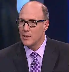 Head and shoulders photograph of Pioli wearing a dark blue suit with a purple patterned tie and black eyeglasses