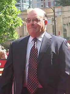 Half-length view of a portly, balding man wearing glasses as he walks down a street