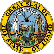 A circular seal with the text "Great Seal of the State of Idaho", along with a white star, within the outer ring. The inner ring contains a banner with the text "Esto perpetua", a woman in white holding a scale, a man dressed as a miner, and an elk's head above a shield containing a natural landscape. Below the woman and man are cornucopias, and a sheaf of grain is located under the shield.