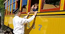 A volunteer conductor greets a child riding in a trolley