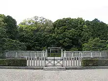 Torii gate behind two concrete fences. In the background there are trees.