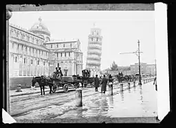 Trucks with material for the ARC village passing the leaning tower.