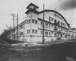 Black and white photo of a three-storey building, constructed in wood with an arched roof and a clock tower