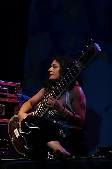 A woman sitting while playing a sitar