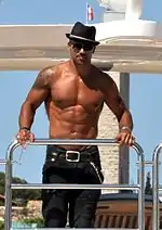 Muscular, shirtless man in sunglasses and black fedora