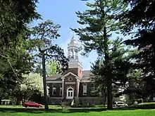 Brown Federal-style brick building with white cupola, photographed through trees