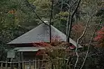 Small hut with thatched pyramid shaped roof amongst trees.