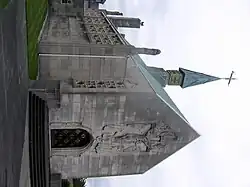 A grey-white stone chapel seen from the northwest, with a central spirelet with a cross. There is an elaborate carving of the Crucifixion over the west door, a tall pinnacle at the corner, and elaborate stone tracery in the windows along the side