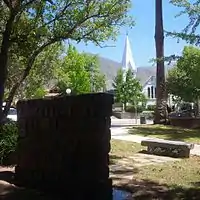 Park at Sierra Madre Blvd and Hermosa looking North. From foreground to background: Weeping Wall Veterans Memorial, Sierra Madre Veterans Time Capsule bench, 1905 World War I Cannon,  Sierra Madre Boulevard, Old North Church built in 1890, a Sierra Madre historic landmark and the San Gabriel Mountains.