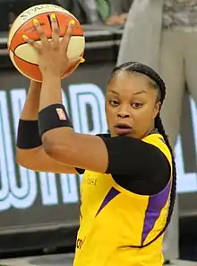 Waist high portrait of young woman holding up a basketball wearing very long braids reaching her waist and a yellow basketball uniform