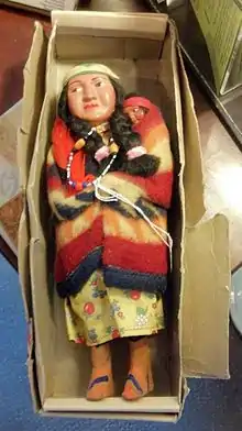 A female Indian doll wrapped in a blanket with a baby, in an old cardboard box