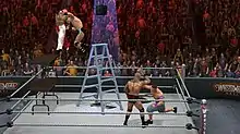 A shirtless masked wrestler attempts to slam a wrestler wearing blue and white striped shorts through two stacked tables, another wrestler waring jean shorts and sneakers punches a fourth wrestler who is holding his head. All four are in a wrestling ring with a ladder at the center and a briefcase hanging above the ladder, in front of a crowd.