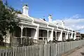 Row of six single storey white terraces with street-facing verandahs