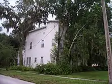 a two-story square building partially obscured by oak trees