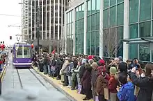 A large crowd of people on a station platform waiting for an approaching streetcar.