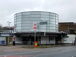 A white building with a rectangular, dark blue sign reading "SOUTH RUISLIP STATION" in white letters all under a light blue sky