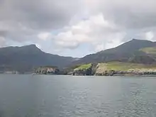 Grey hills back green moors beyond a grey body of water. A small island is separated from the cliffs of the shore by a deep chasm.