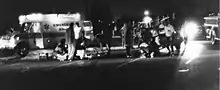 Several emergency personnel in a night-time scene, clustered around a person lying on the floor.