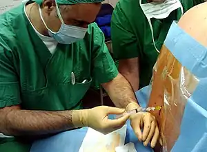 A man injects a clear liquid through a tube into the patient's spine