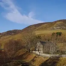 A stone church with a path beside it, and hills in the background.