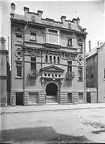 Old photo of the front of the former Hall showing its complex details. It was built of brick with a rusticated basement, balconies with curved wrought iron balustrades, a large entrance stairway under a prominent pediment and Art Nouveau panels.