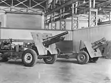 Two artillery guns mounted on wheeled gun carriages photographed inside of a building. The weapons have a large plate mounted about halfway down the length of their barrels.