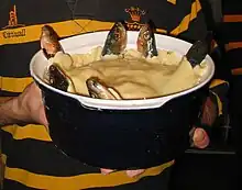 A blue ceramic dish containing a stargazy pie, with six fish poking out of a shortcrust pastry lid, looking skywards (from Culture of Cornwall)