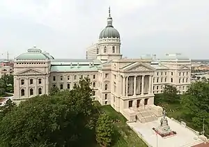 A view looking down on a large building made of limestone. It is three stories high with two wings sweeping out from a central atrium with a domed stained glass roof