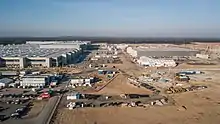 Giga Berlin-Brandenburg under construction in Grünheide, on the edge of a highway with a industrial park in the distance