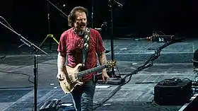Johnston playing a Paul Reed Smith Artist's Gold Top while wearing a black t-shirt and jeans, in front of colorful stage lights