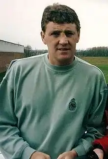 A brown-haired man in a light green sweatshirt with a neutral expression