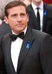 Image of Steve Carell wearing a black bow-tie with his tuxedo, standing on the red carpet at the 2017 Academy Awards. He is wearing a blue ribbon in his lapel to show his support for the American Civil Liberties Union. The photograph shows Carell's head and torso.