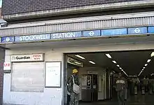 A brown-bricked building with a rectangular, light blue sign reading "STOCKWELL STATION" in white letters all under a light blue sky