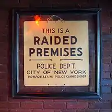 A framed sign on a brick wall. It reads, "THIS IS A RAIDED PREMISES. POLICE DEP'T. CITY OF NEW YORK. HOWARD R. LEARY. POLICE COMMISSIONER".