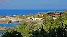 A large wooden building on a rocky promontory with sea and surf in the background